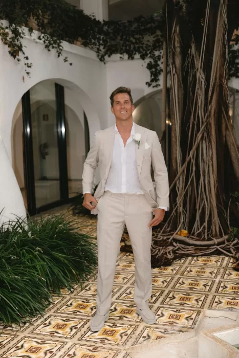 Groom posing confidently in a light suit near the vine-covered courtyard of Hacienda Na Xamena.