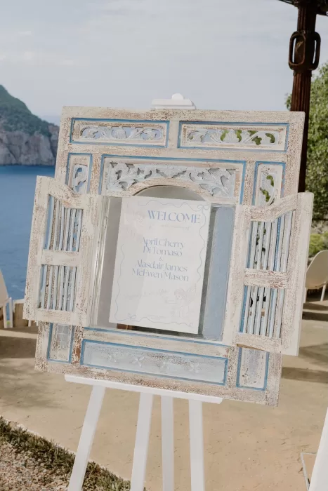 Ornate blue-and-white wedding welcome sign displayed in a carved frame with the sea behind it at Hacienda Na Xamena.
