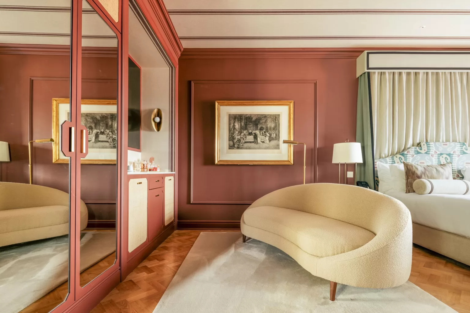 Sophisticated bedroom at Hospes Infante Sagres featuring a curved beige sofa, rich red walls, and gold-framed artwork for a timeless ambiance