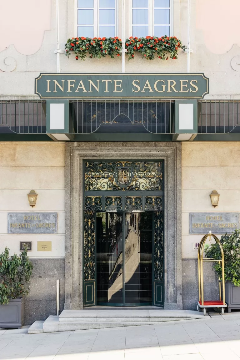Exterior entrance of Hospes Infante Sagres with green and gold signage, decorative wrought iron door, and flower boxes above.