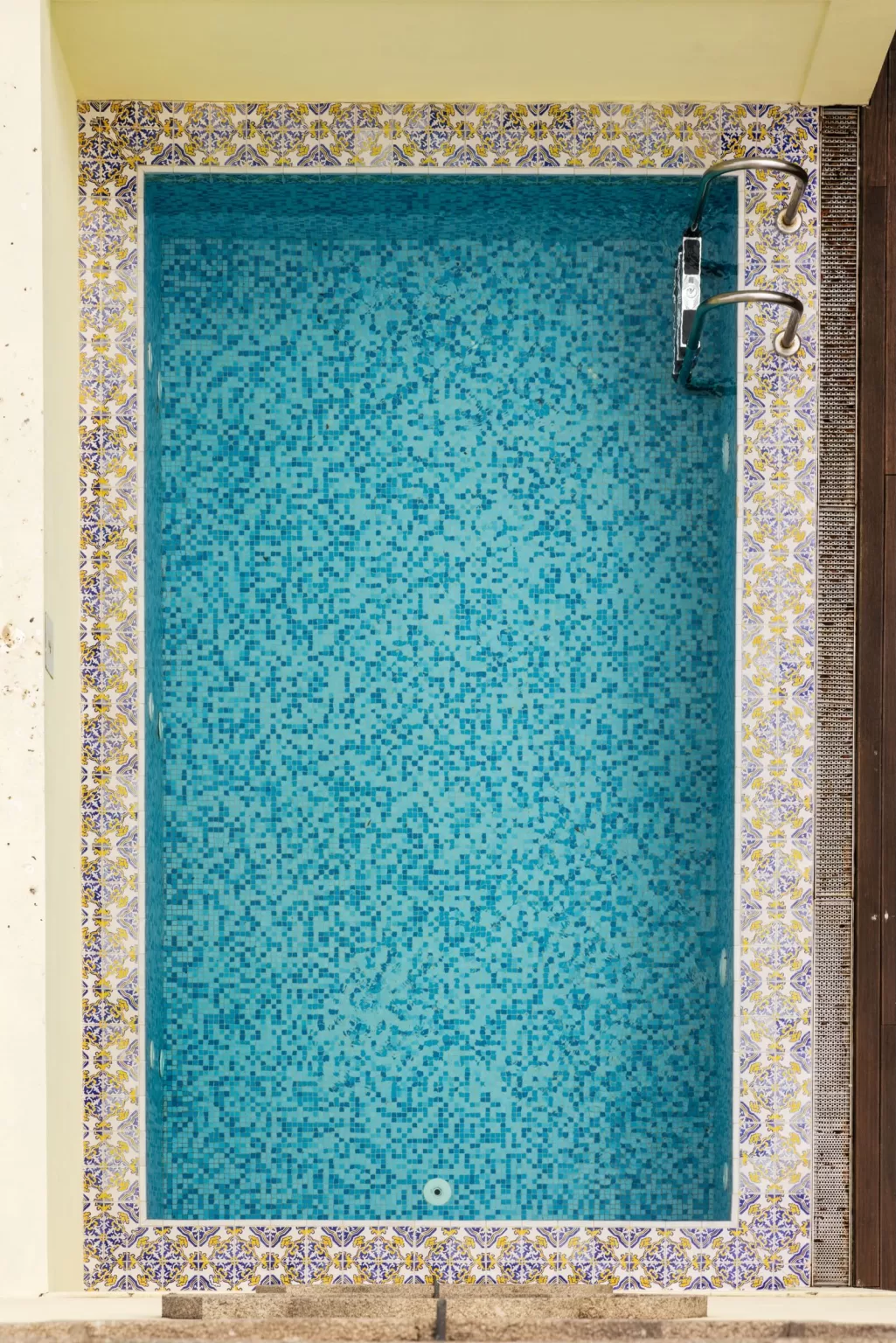 Close-up of the mosaic-tiled pool at Hospes Infante Sagres, bordered by patterned Portuguese tiles in yellow and blue.