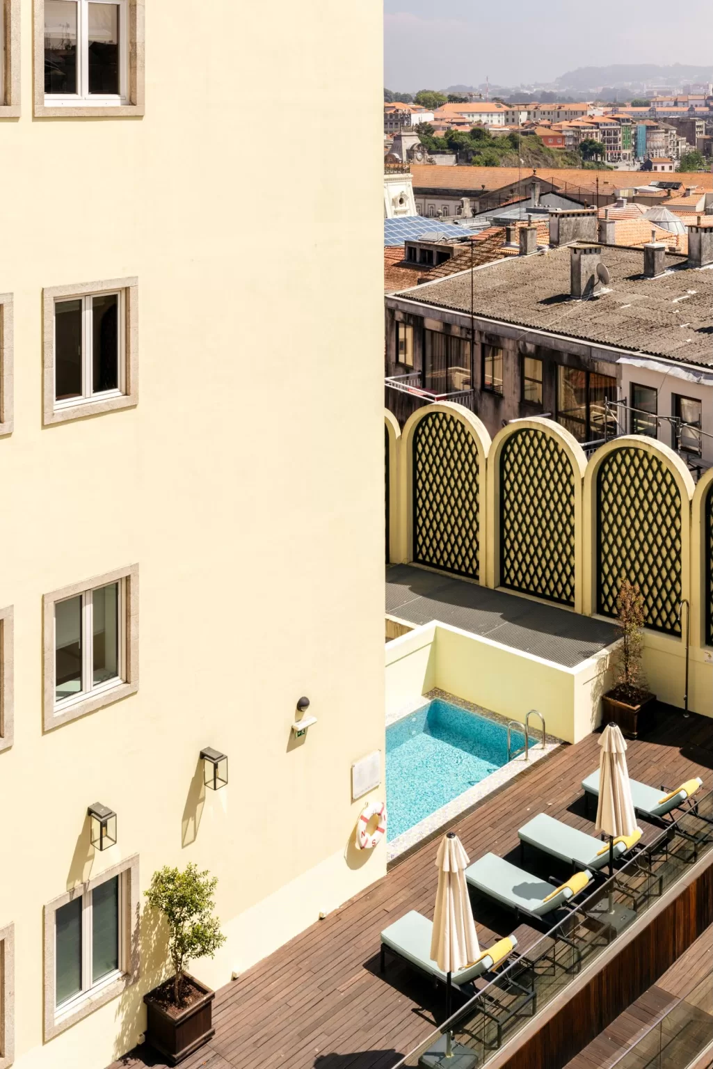 Rooftop pool terrace at Hospes Infante Sagres overlooking Porto’s historic rooftops, featuring sun loungers and soft yellow walls.
