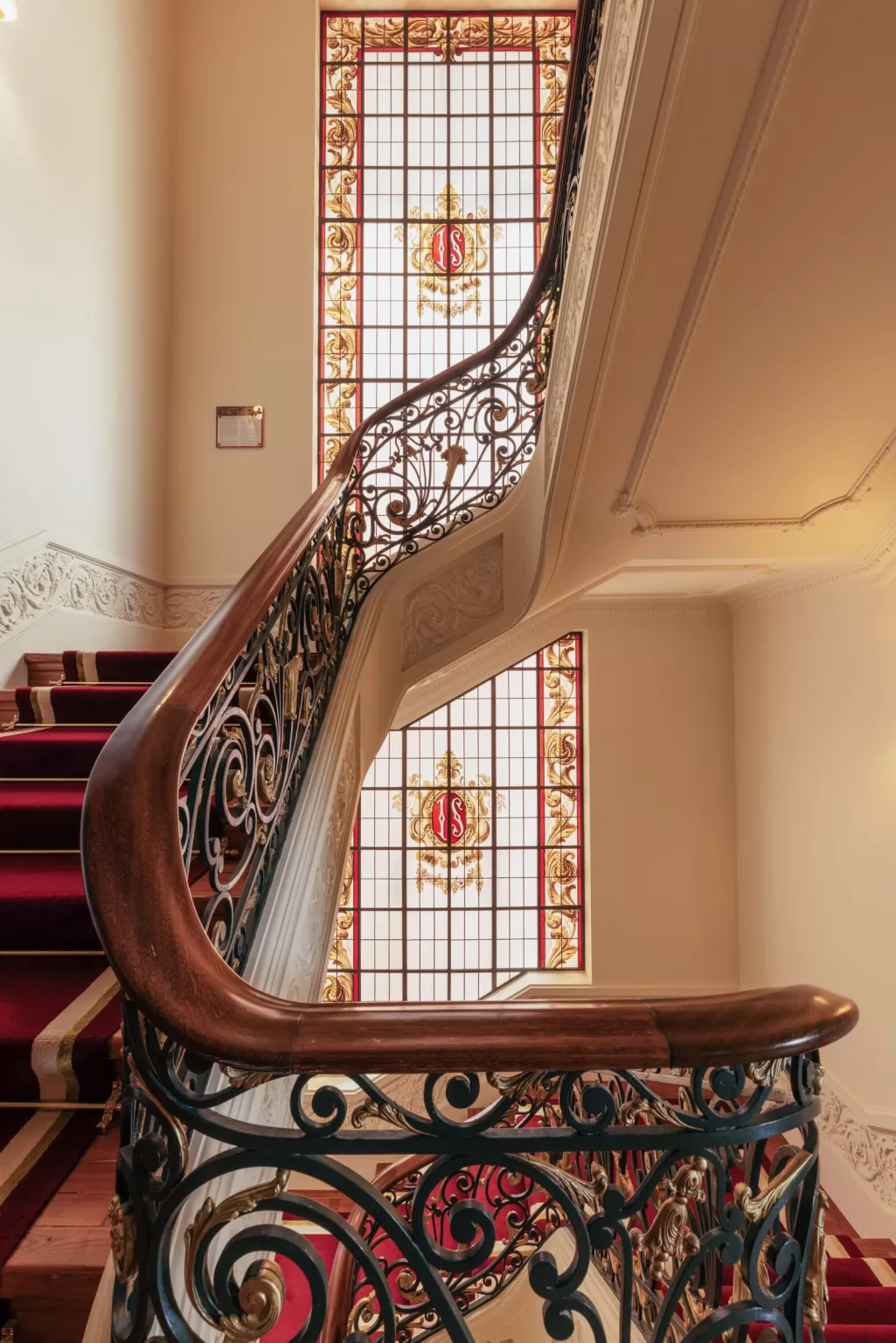 Ornate staircase at Hospes Infante Sagres with red carpet and decorative wrought iron railings beside a stained glass window.