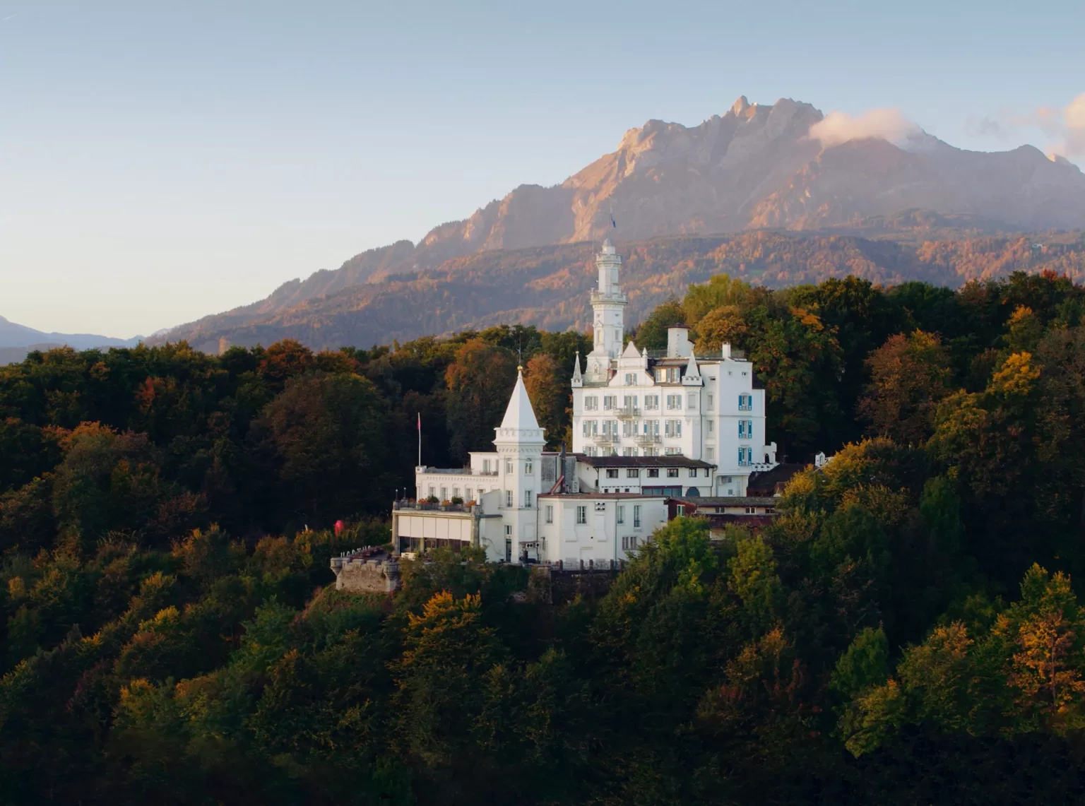Hotel Château Gütsch surrounded by autumn trees with the Swiss mountains rising in the background.