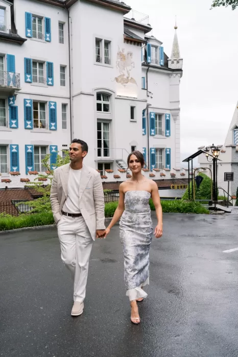 Couple walking hand in hand outside Hotel Château Gütsch, framed by its blue shutters and fairytale façade.