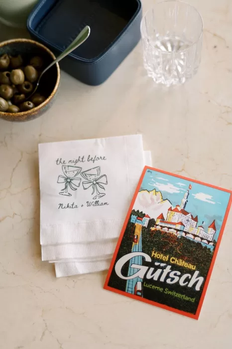 Close-up of custom wedding napkins and a vintage Hotel Château Gütsch postcard placed on a marble table.