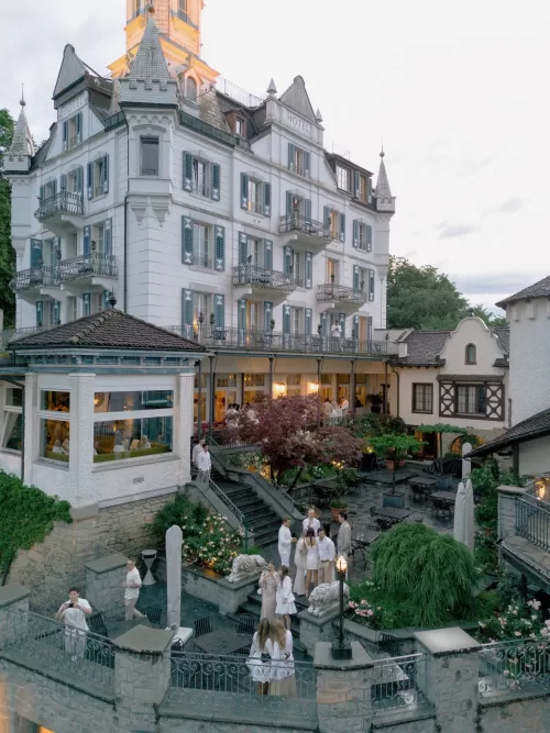Guests dressed in white gather on the elegant stone terrace of Hotel Château Gütsch at dusk.