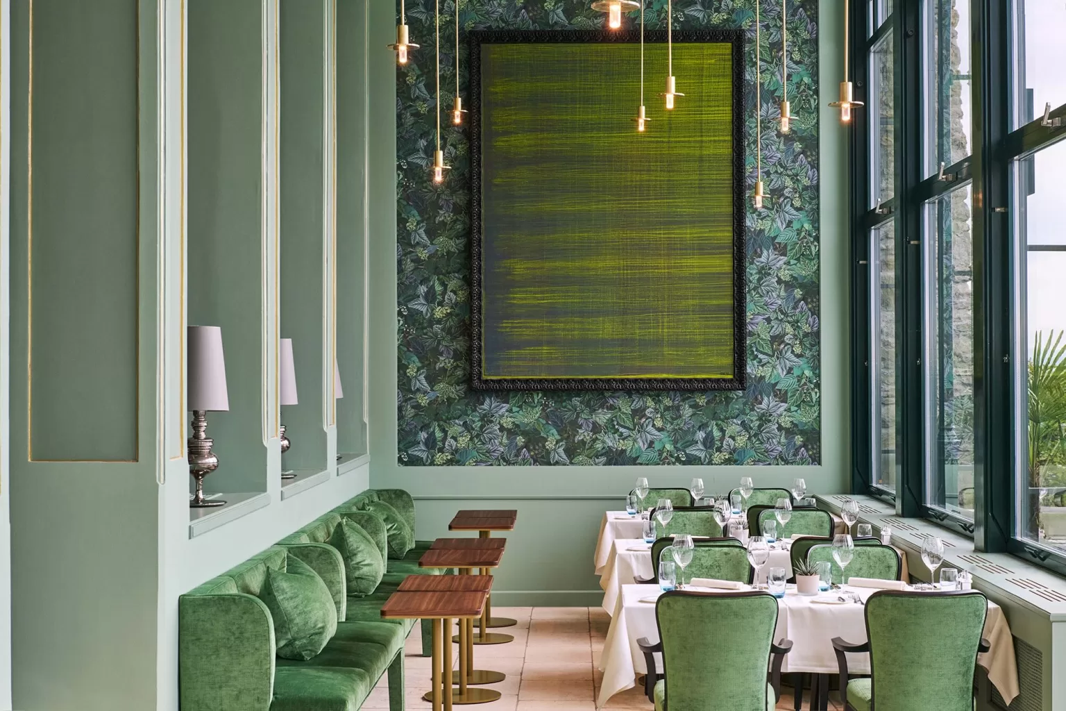 Stylish green dining room at Hotel Château Gütsch with velvet seating, botanical wallpaper, and modern pendant lights.