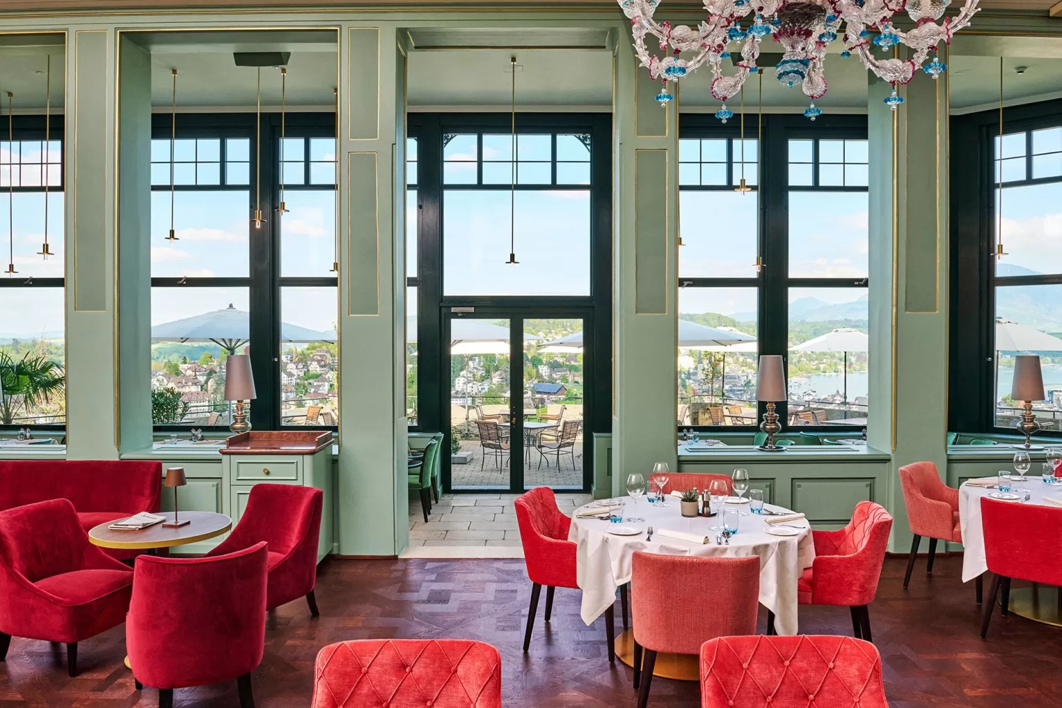 Elegant restaurant at Hotel Château Gütsch with red velvet chairs, mint-green walls, and large windows overlooking Lucerne.