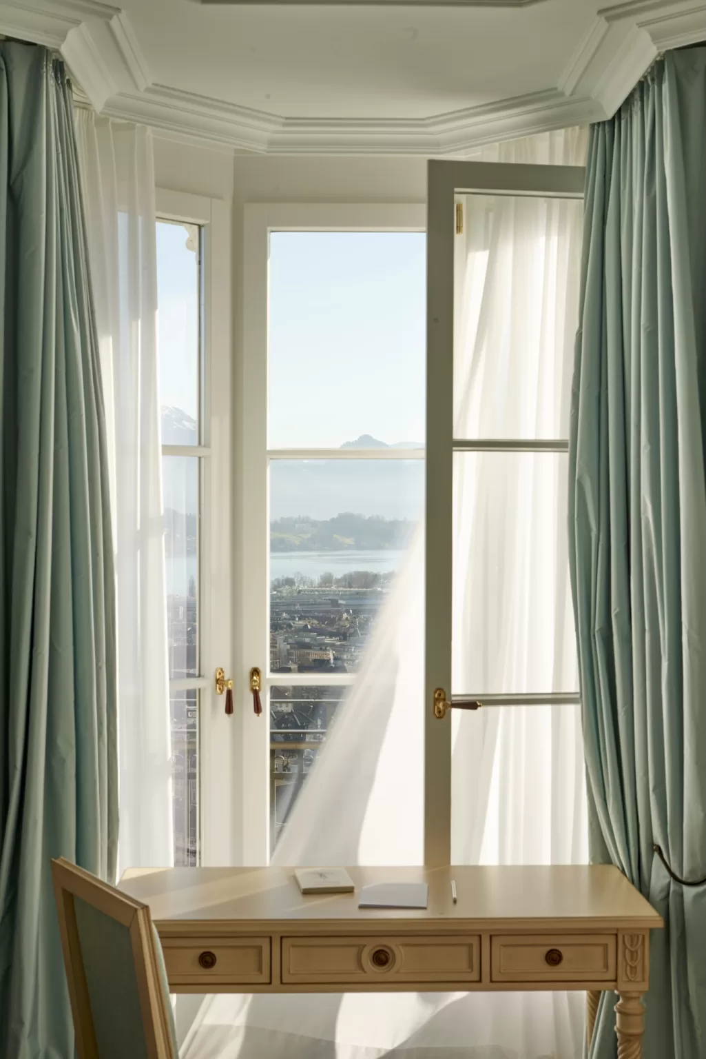 Peaceful writing desk beside an open window with flowing curtains and mountain views at Hotel Château Gütsch.