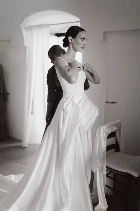 Bride adjusting her gown while getting ready inside a softly lit room at Masseria Spina.