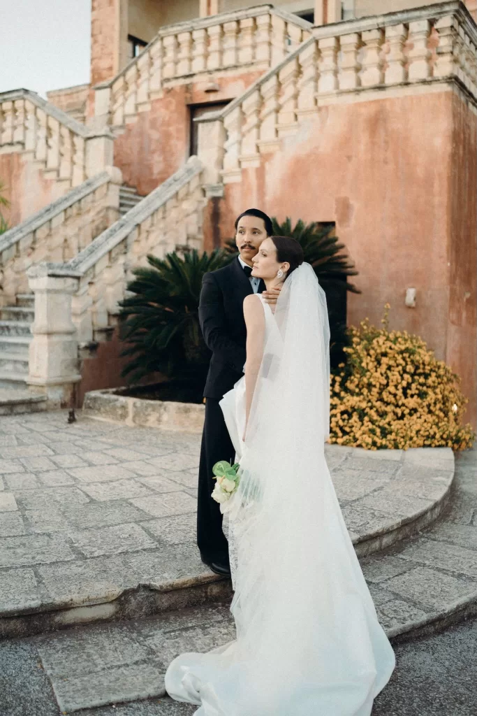 Wedding couple posing together in front of the terracotta façade and stone staircase of Masseria Spina.