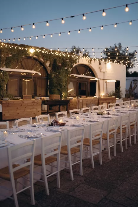 Long candlelit dinner tables set beneath string lights in the courtyard of Masseria Spina.