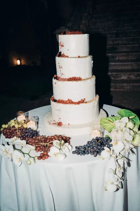 Four-tier wedding cake decorated with berries, orchids, and candlelight during the Masseria Spina reception.