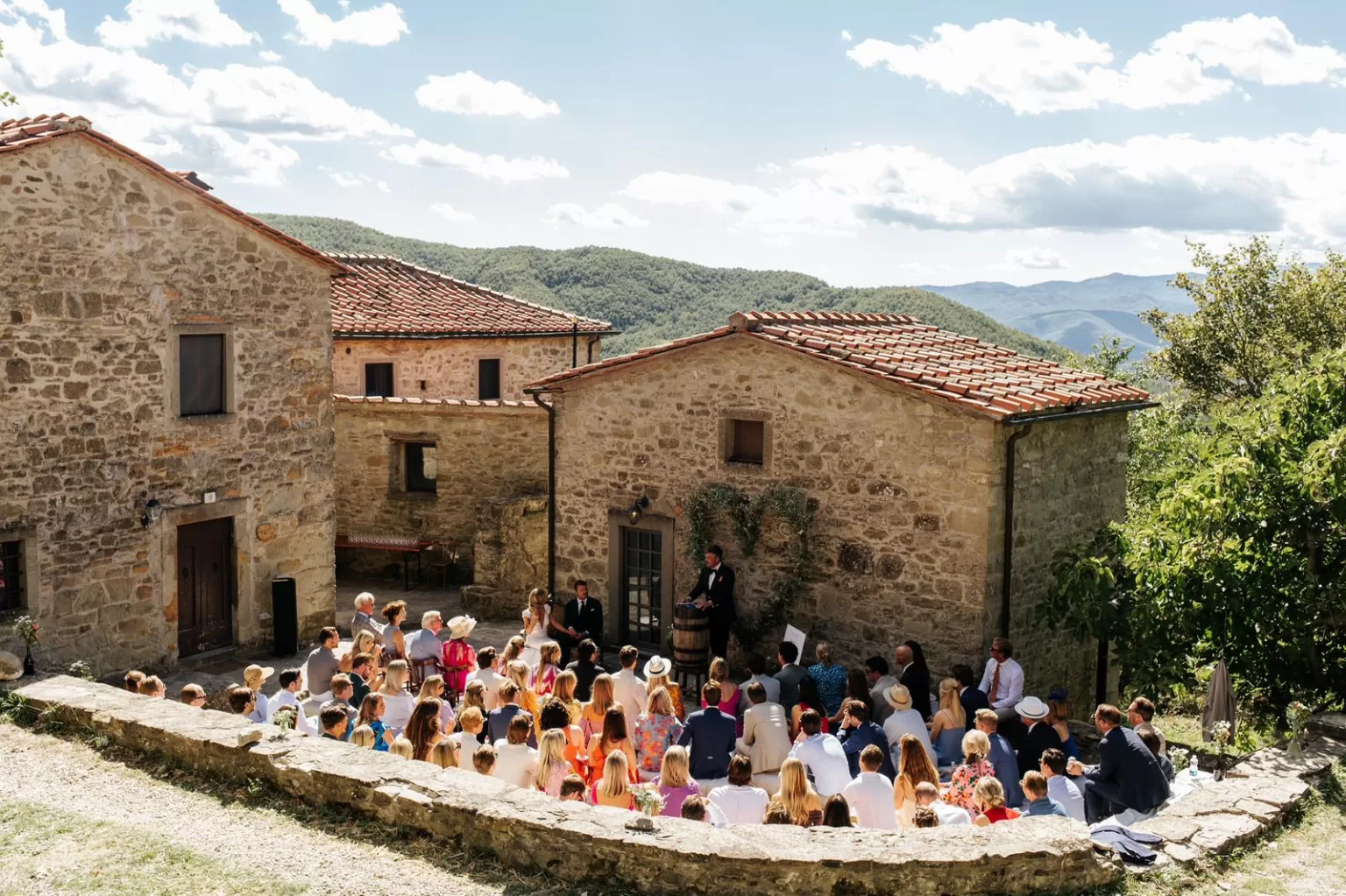 Courtyard wedding ceremony at Novanta 90 surrounded by stone buildings and rolling green hills.