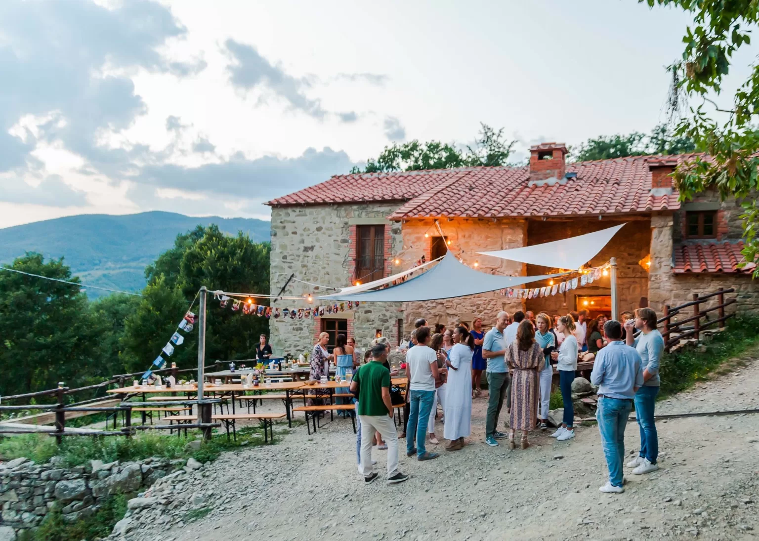 Evening celebration with string lights and long tables outside the stone farmhouse at Novanta 90.