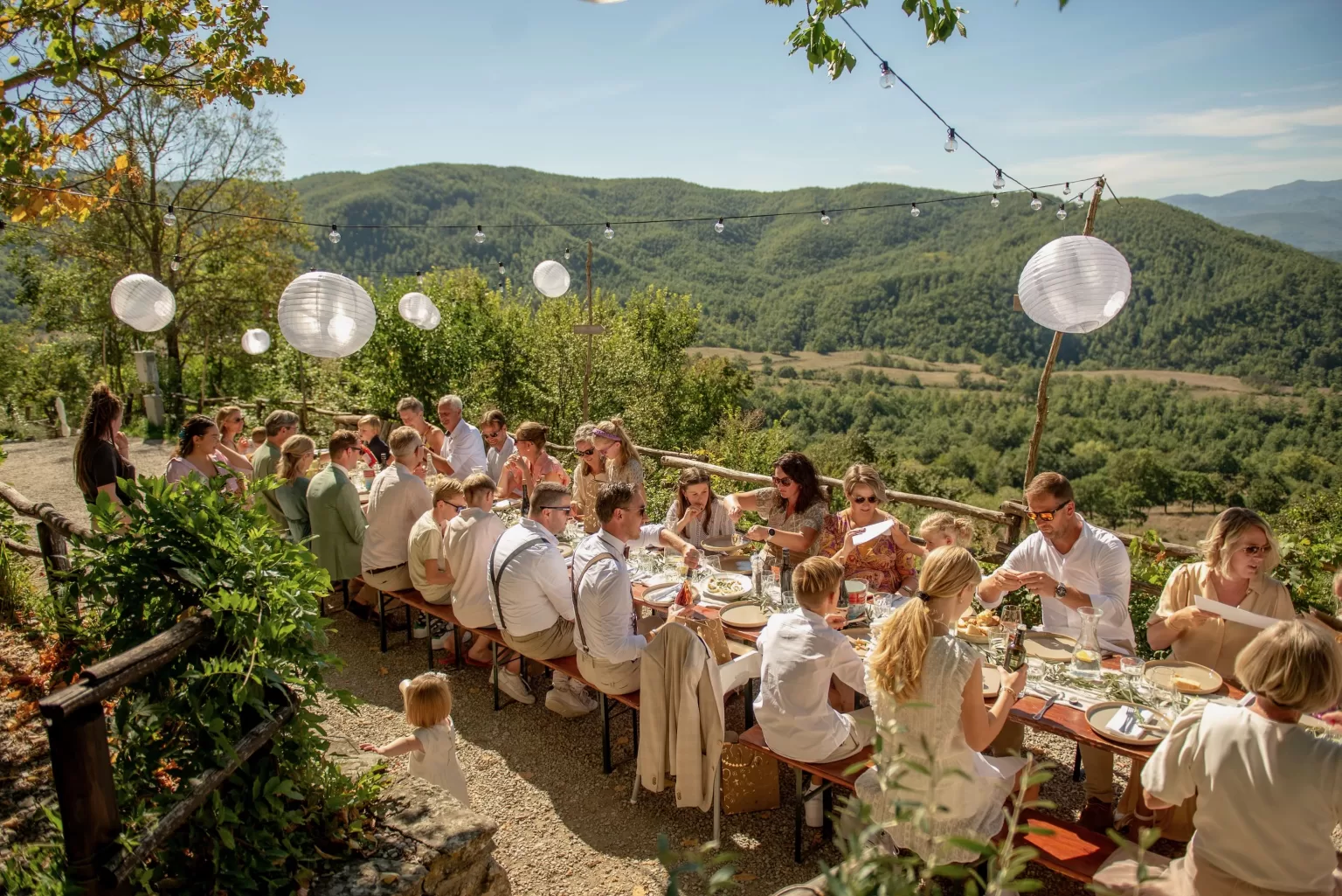 Guests enjoying a sunlit family-style lunch overlooking Tuscan hills at Novanta 90.