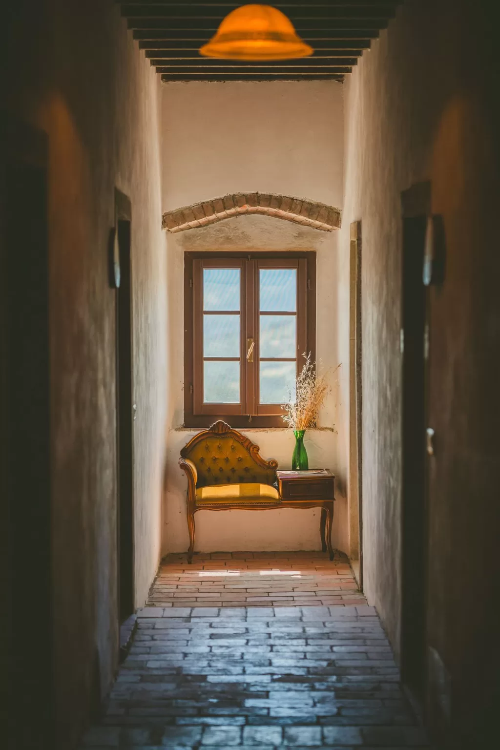 Warm rustic hallway at Novanta 90 with a yellow velvet chair and natural light streaming through the window