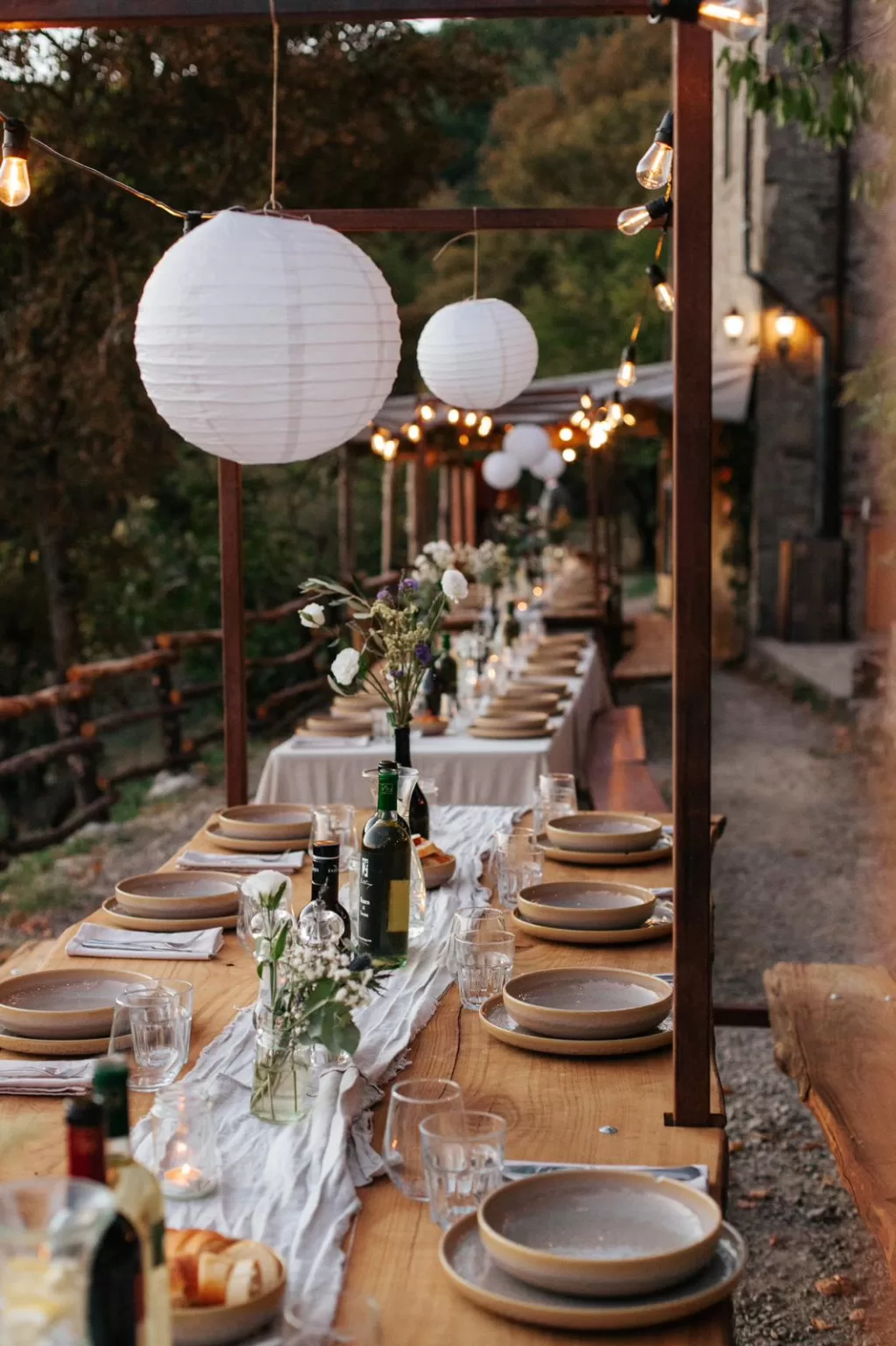 Long wooden dinner table at Novanta 90 set under hanging lanterns and string lights for an intimate evening celebration.