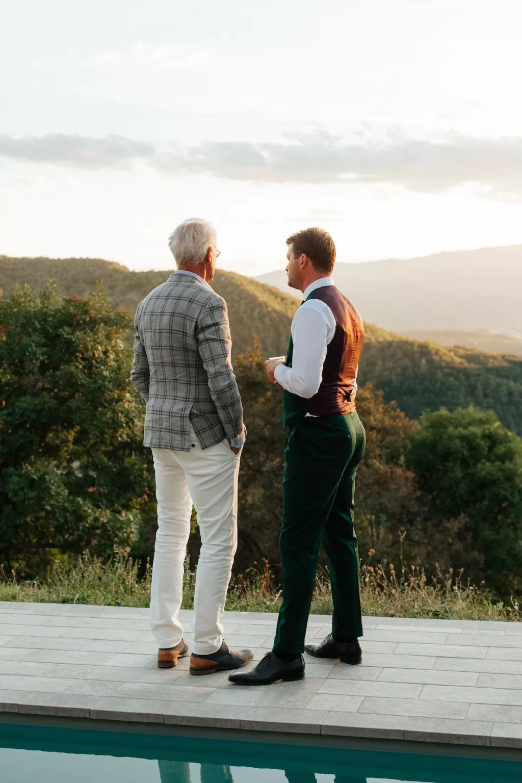 Two men in suits chatting by the pool at Novanta 90 as the sun sets over the Tuscan hills.