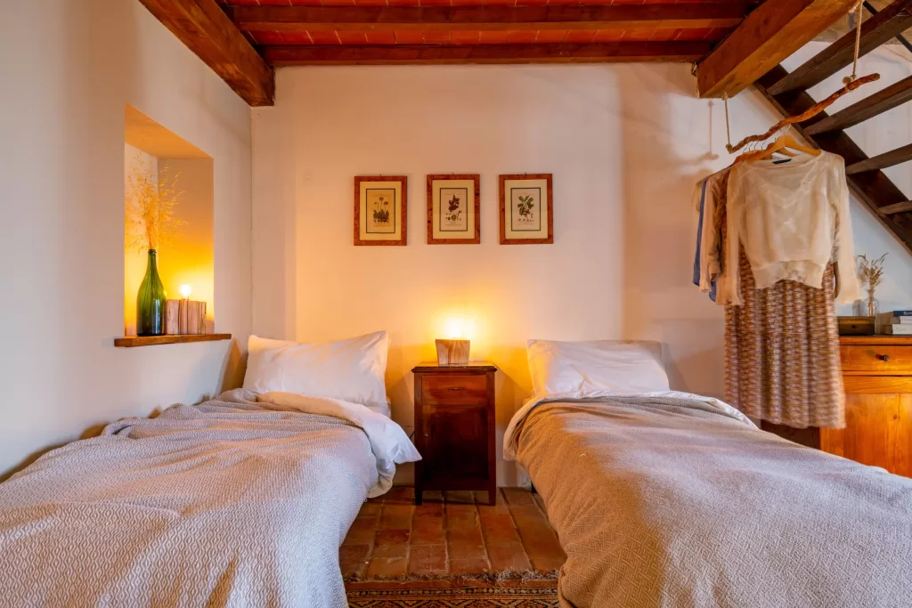 Cozy twin bedroom at Novanta 90 with soft lighting, rustic beams, and warm terracotta floors.