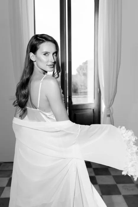 The bride in a flowing robe at Apulien Bari, turning toward the camera as sunlight fills the room behind her.