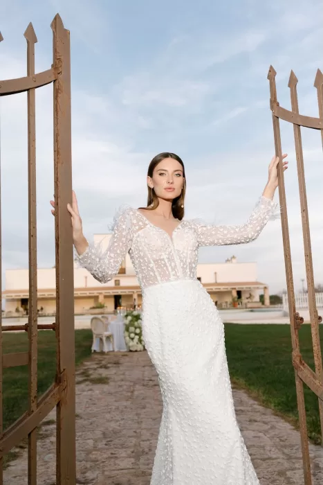 A bride posing between rustic iron gates at Apulien Bari, her embroidered gown catching the late-day light.