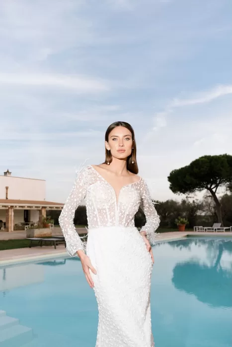 Bride in a sheer embroidered gown posing by a serene pool at a wedding in Apulien, Bari.