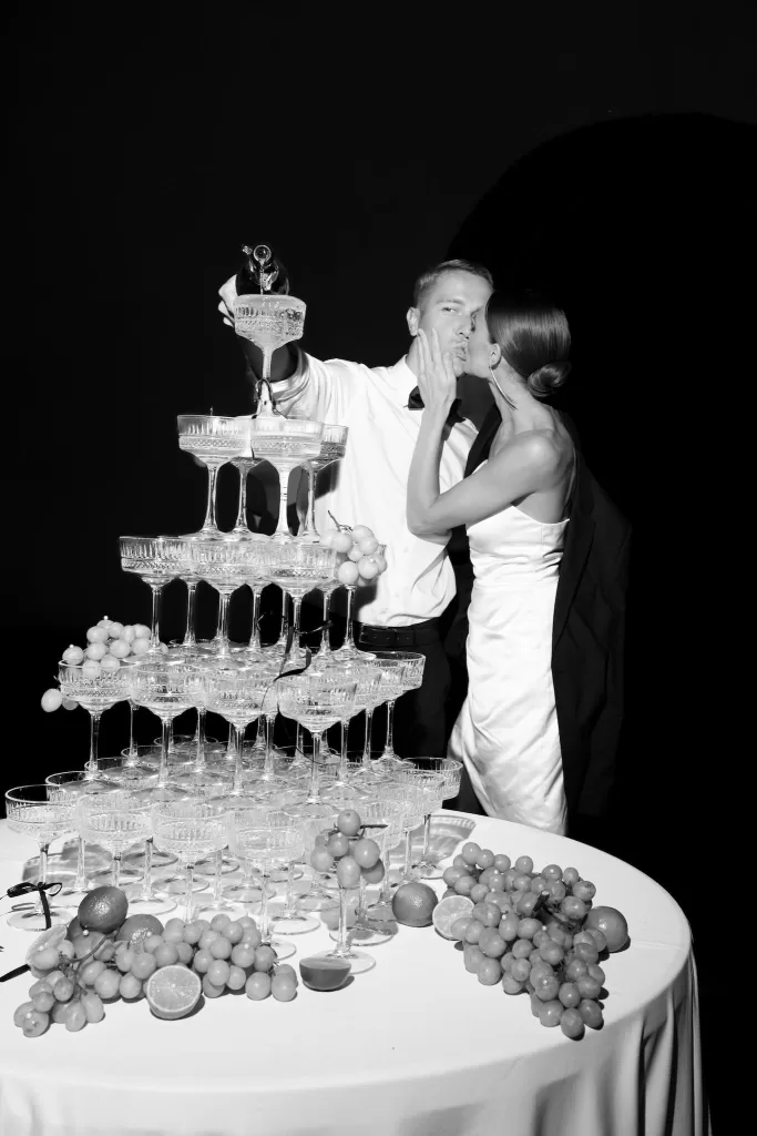 A romantic moment as the couple kisses beside a champagne tower at Apulien Bari during their nighttime celebration.