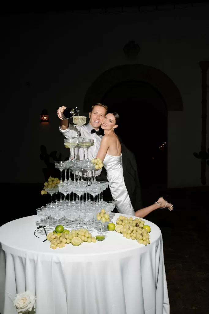 The bride and groom pouring champagne over a tall glass tower at Apulien Bari, surrounded by grapes and evening ambience.