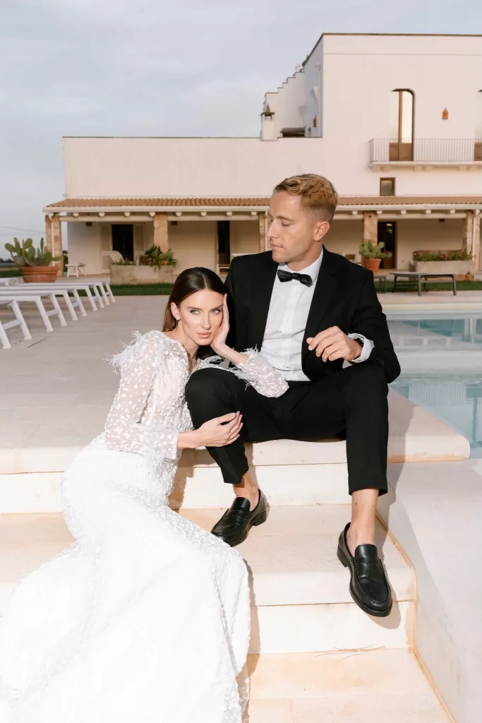 Bride resting on groom’s leg as they sit on sunlit poolside steps in Apulien, Bari.