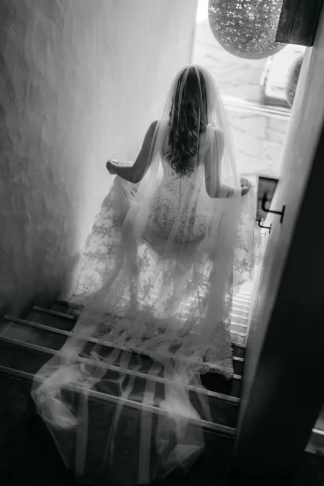 Bride walking down interior stairs at Areias do Seixo, her veil flowing softly behind her.