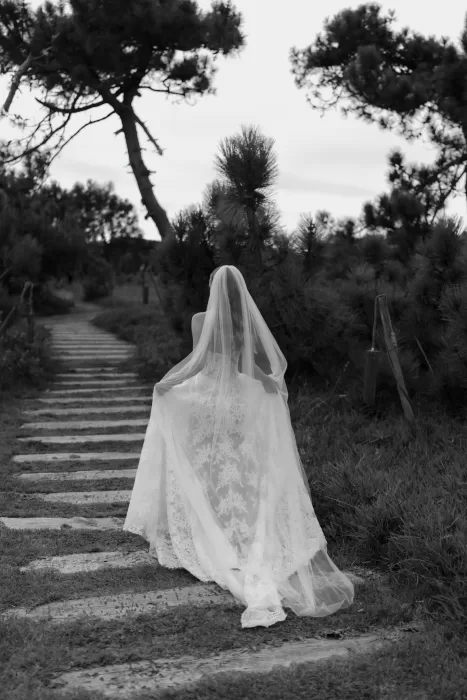 Bride seen from behind walking along a garden path at Areias do Seixo, her veil flowing through the natural landscape.