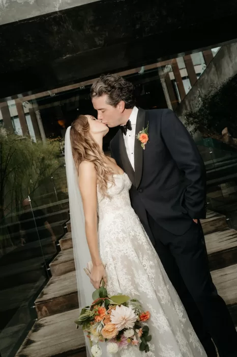 Bride and groom kissing beside the modern glass and concrete architecture at Areias do Seixo.