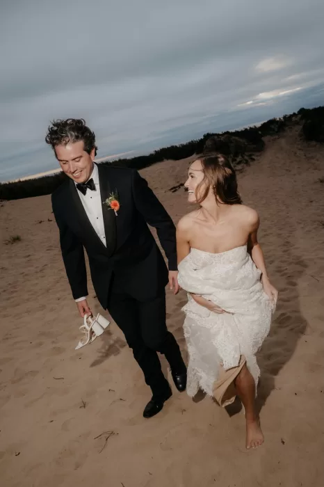 Bride and groom walking barefoot through the sand dunes at Areias do Seixo, relaxed and smiling together.