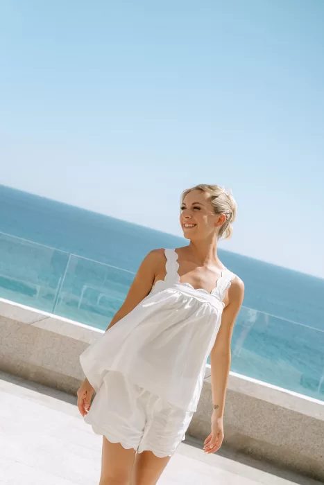 Bride in a white pre-wedding outfit smiling on a terrace overlooking the ocean near Baja Luna.