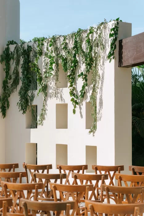 White sculptural ceremony wall at Baja Luna with trailing greenery and wooden chairs set for an outdoor wedding.