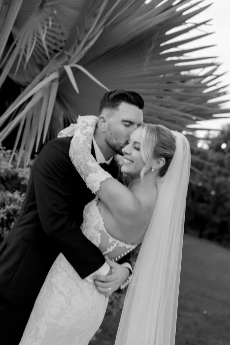 Intimate black and white portrait of the bride and groom embracing beneath palm trees at Baja Luna.