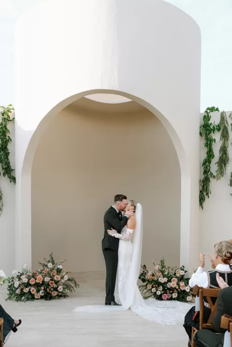 Bride and groom sharing their first kiss during the ceremony at Baja Luna beneath the arched altar.