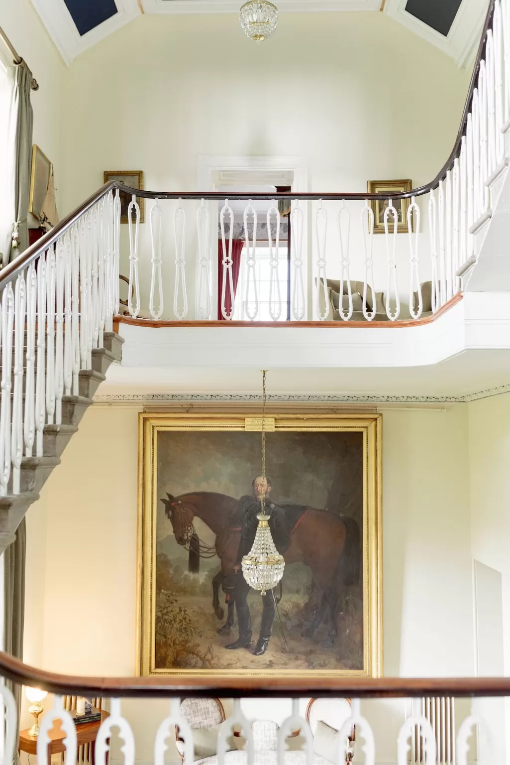 Grand staircase inside Boturich Castle with white balustrades, chandelier lighting and classic portrait artwork creating an elegant, historic atmosphere.