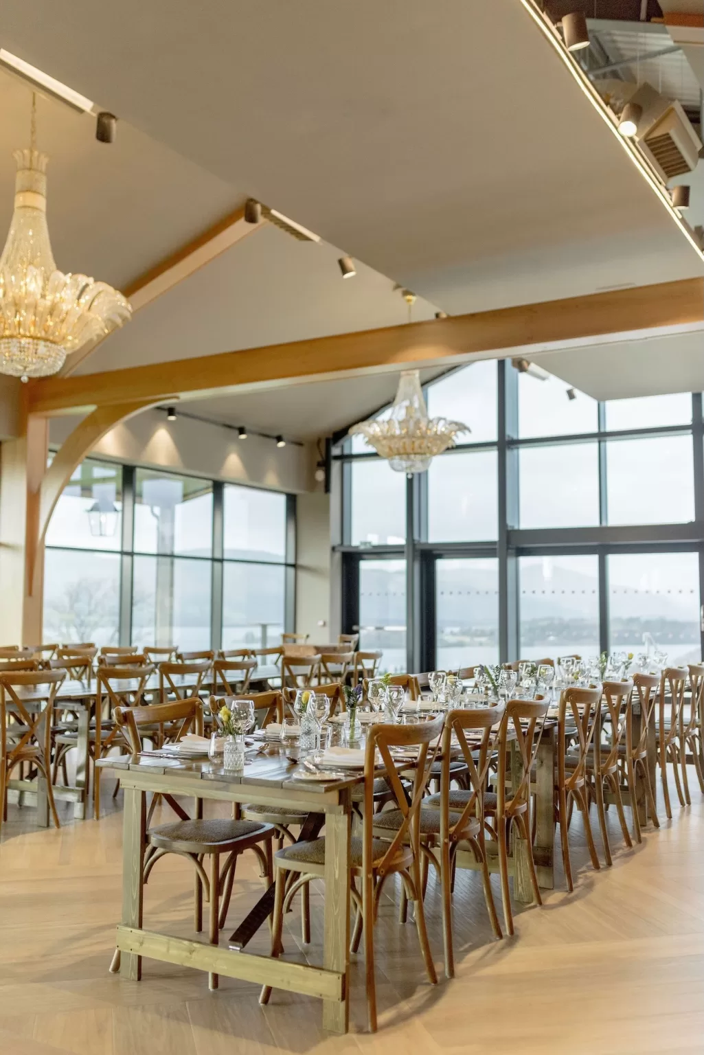 Wedding reception setup inside the Boturich Pavilion with long banquet tables, chandeliers and expansive loch views through large windows.