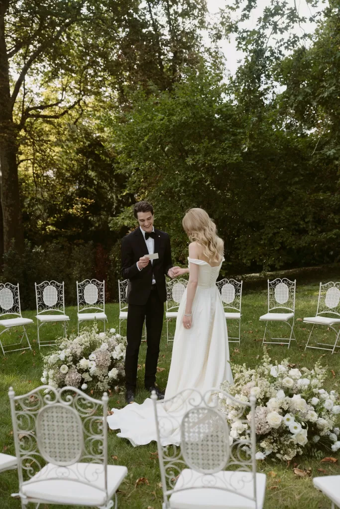 Outdoor wedding ceremony at Château du Prieuré d’Evecquemont with white chairs and floral arrangements in a garden setting.