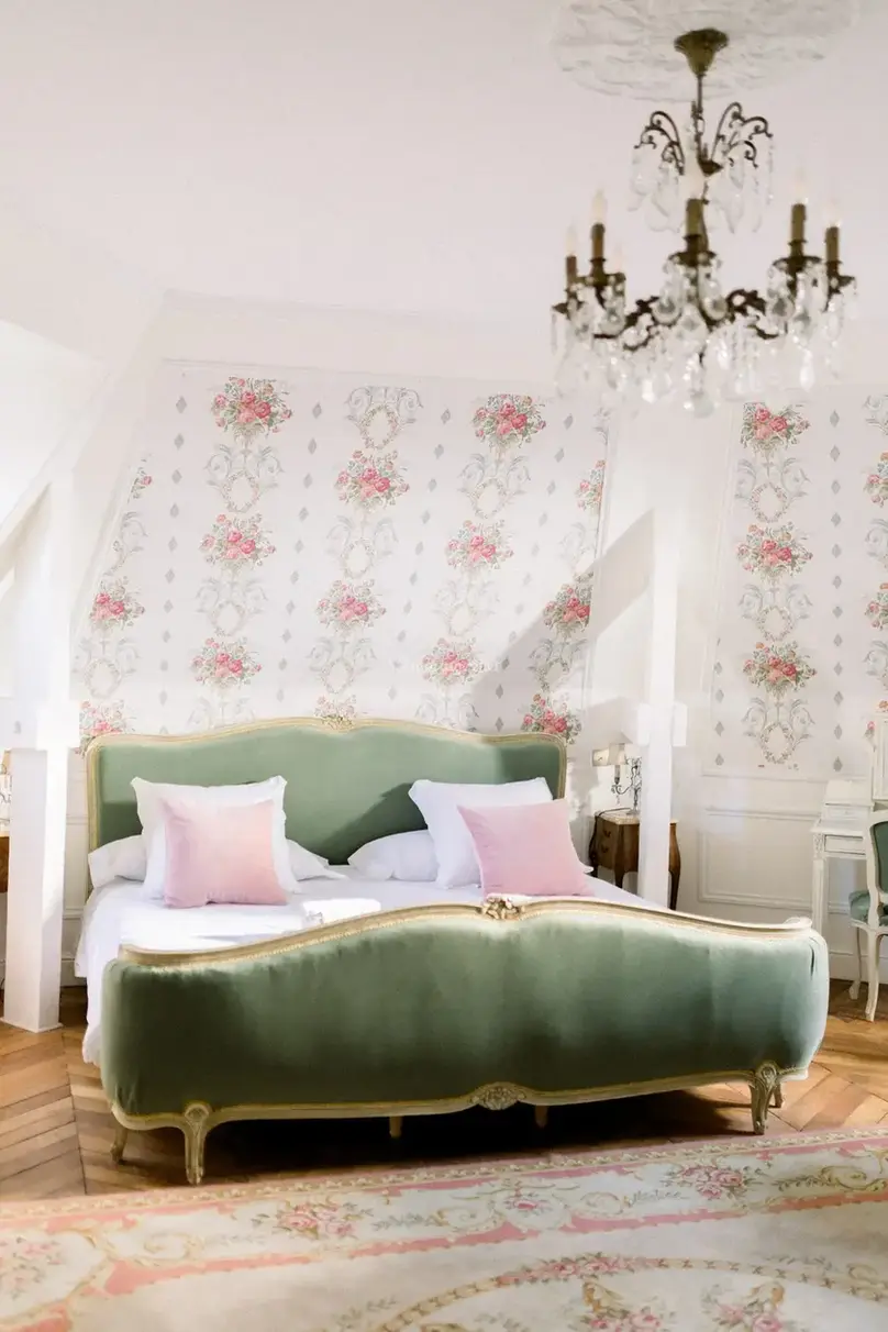 Romantic bedroom at Château du Prieuré featuring a green velvet bed, floral wallpaper, and soft morning light.