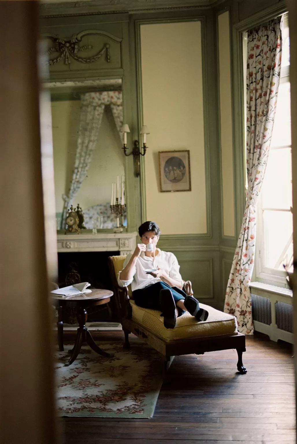 Groom lounging on a chaise with a cup of coffee in a softly lit room at Château du Prieuré.