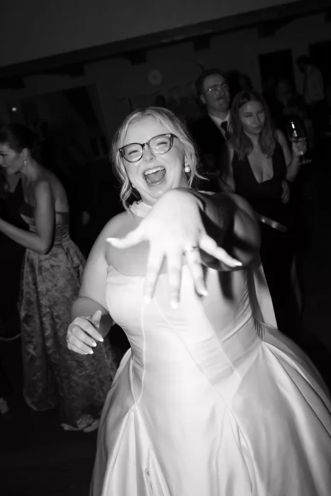 Black and white image of the bride dancing joyfully during the evening reception at Chateau Lill, reaching toward the camera as guests celebrate behind her.