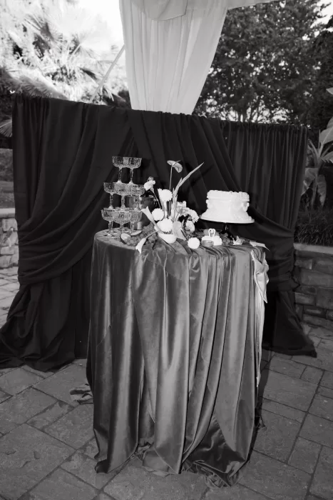 Wedding cake table styled with florals, champagne glasses and draped fabric during an outdoor reception at Chateau Lill.