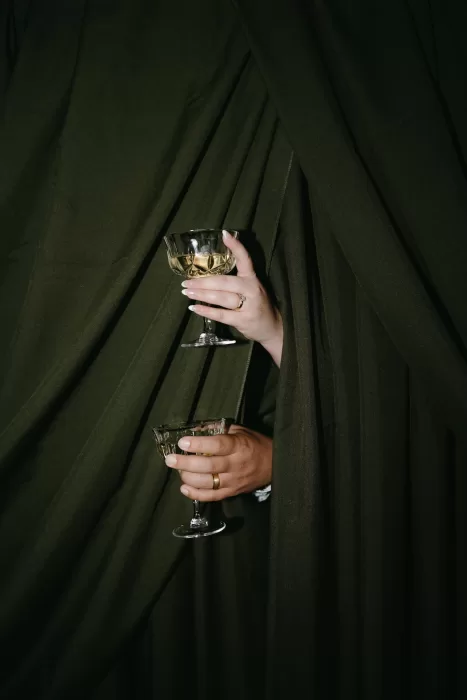 Close-up of the couple’s hands holding coupe glasses of champagne against rich green drapery at Chateau Lill.