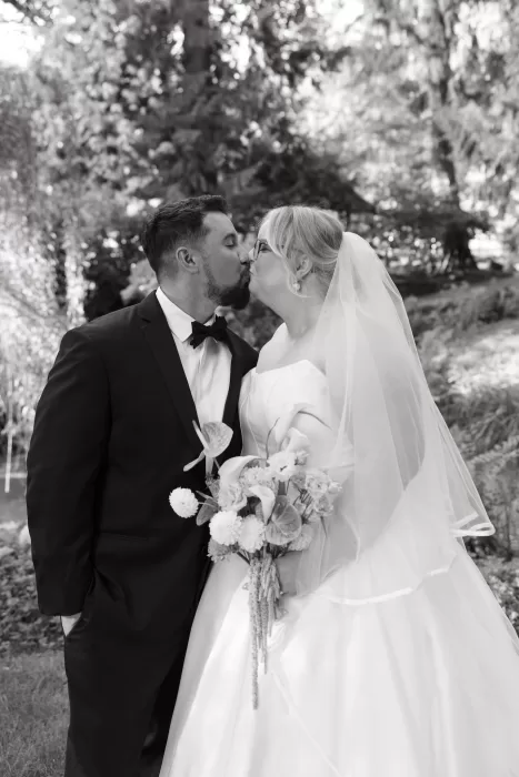 Black and white portrait of the newlyweds kissing in the gardens at Chateau Lill, surrounded by soft foliage.