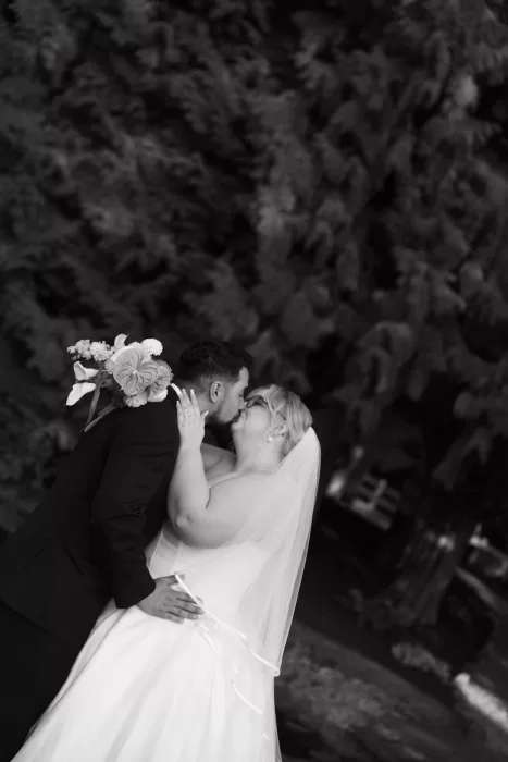 Intimate black-and-white portrait of the couple sharing a kiss outdoors at Chateau Lill, surrounded by lush greenery.