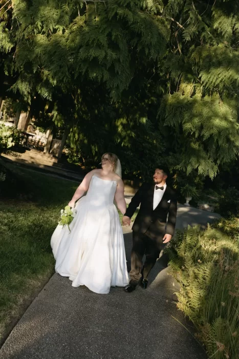 Bride and groom walk hand in hand along a tree-lined path at Chateau Lill, bathed in warm afternoon light.